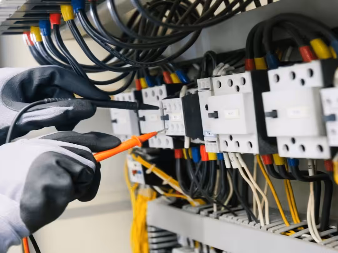 Electrician testing electrical equipment and wiring inside a control panel.