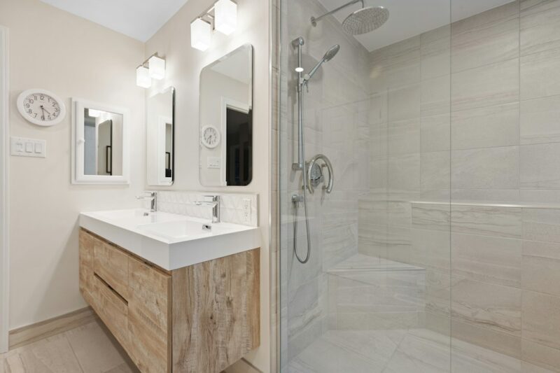 Bright bathroom featuring a wooden vanity against neutral tile floors enhancing warmth and spaciousness.