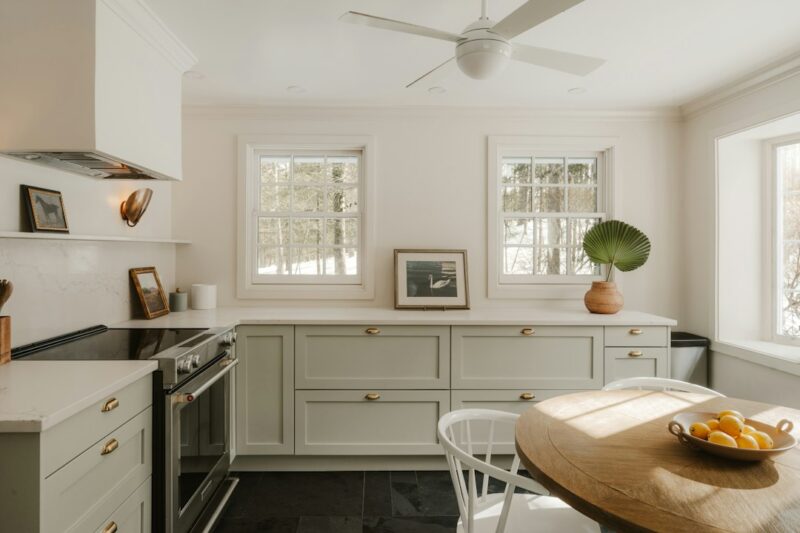 Bright kitchen with light green cabinets and wooden table.