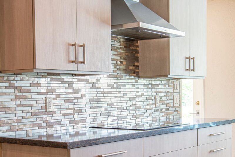 Sleek modern kitchen showcasing white cabinetry paired with a glossy glass tiled backsplash in a herringbone pattern - photo by Derwin Edwards