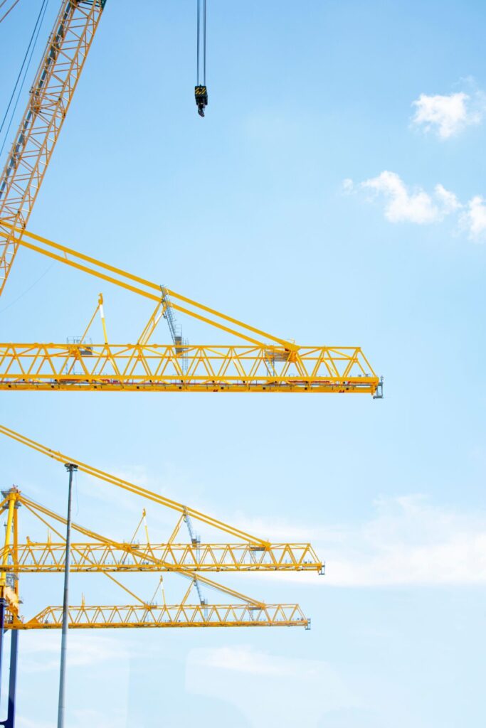 Yellow tower cranes in a construction site reaching into a clear blue sky, symbolizing modern industry.