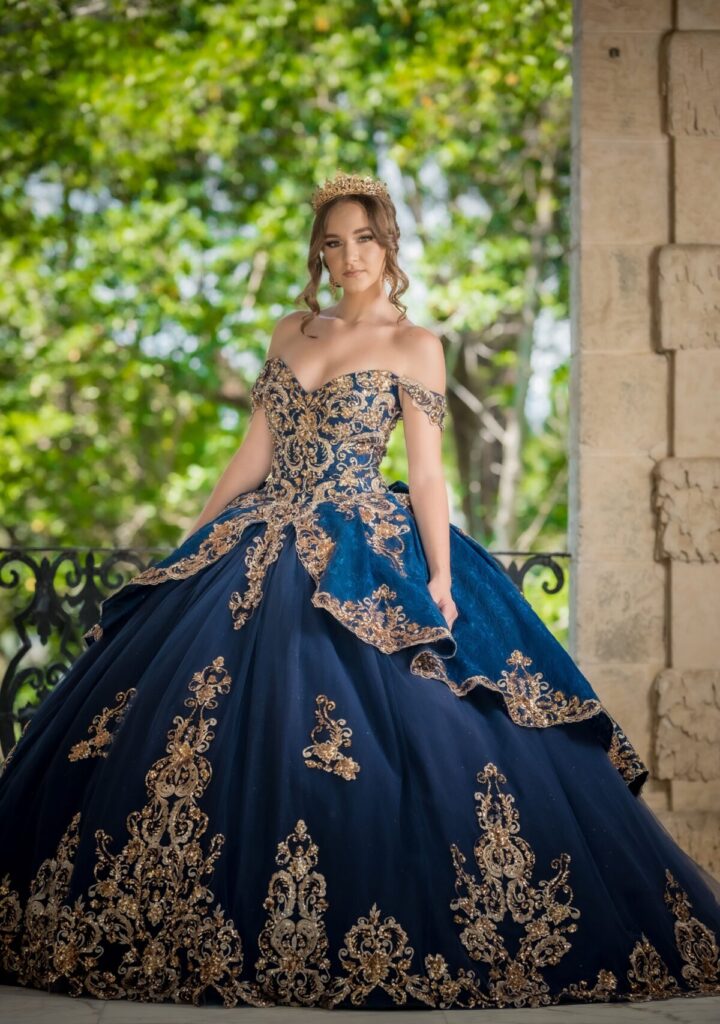 A woman in a royal blue ball gown with ornate details stands elegantly outdoors.