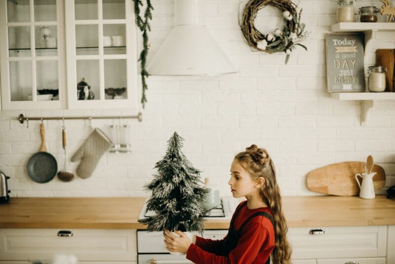 Young girl decorating a cozy kitchen with a mini Christmas tree, capturing the holiday spirit indoors.