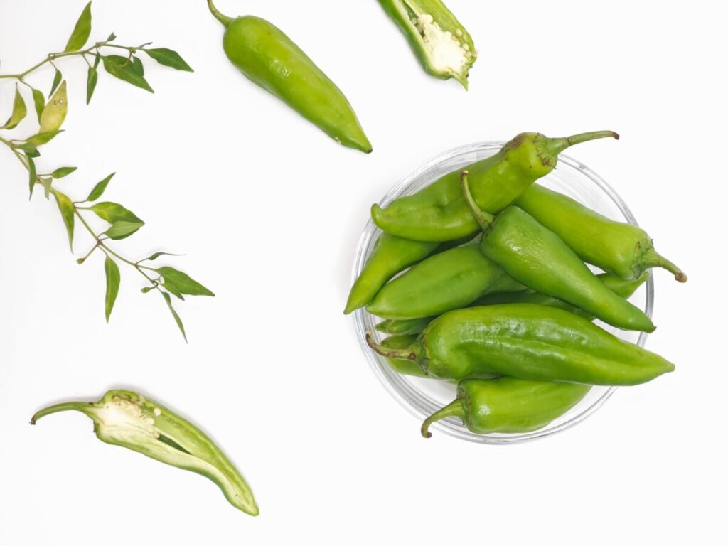Top view of fresh green Anaheim peppers and leaves on white background.