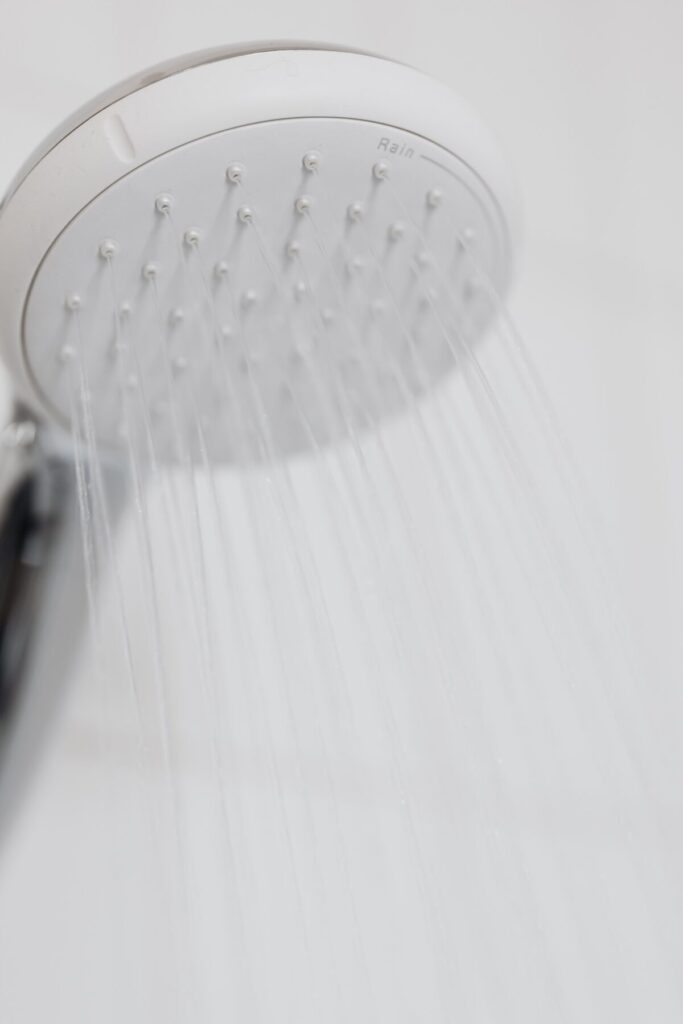 Close-up of a modern shower head with water streaming in a white bathroom setting.