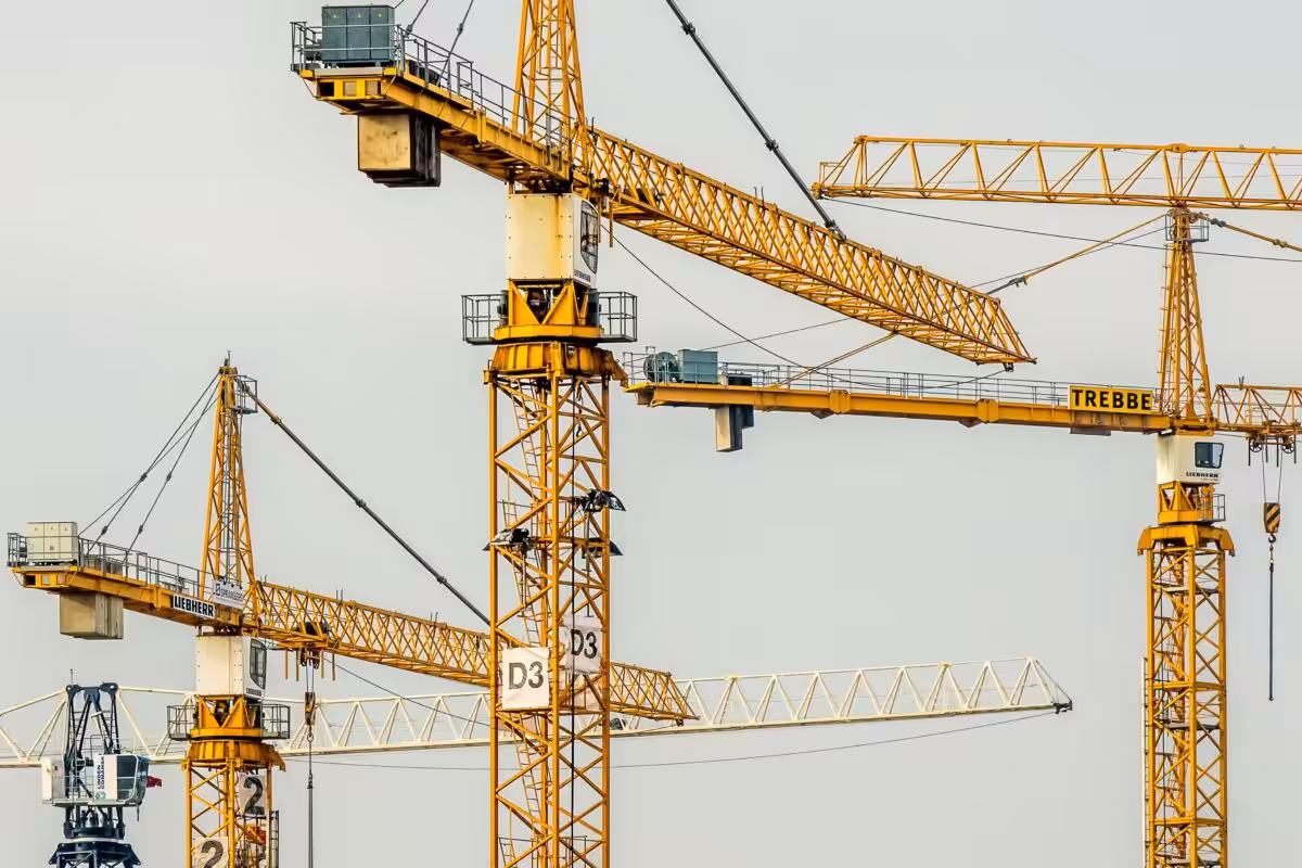 Cluster of yellow tower cranes at a construction site with a gloomy sky background.