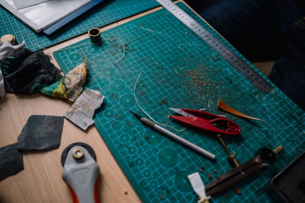 A cluttered craft workspace with various DIY tools and materials on a cutting mat.