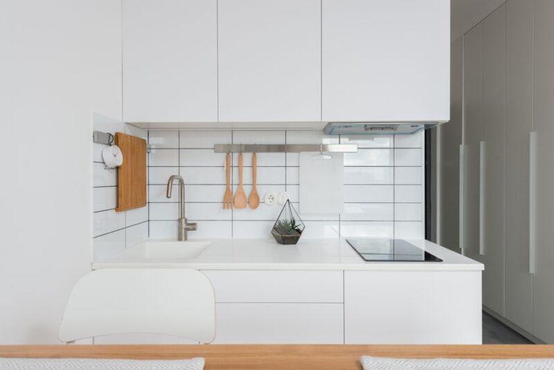 Minimalist kitchen interior combining white cupboards with soft pastel-glazed ceramic tile backsplash for a gentle color accent - photo by Max Vakhtbovych