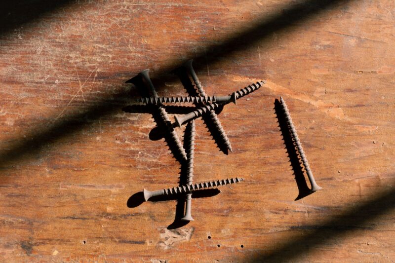 Close-up of rusty screws scattered on a wooden surface with dramatic shadows.