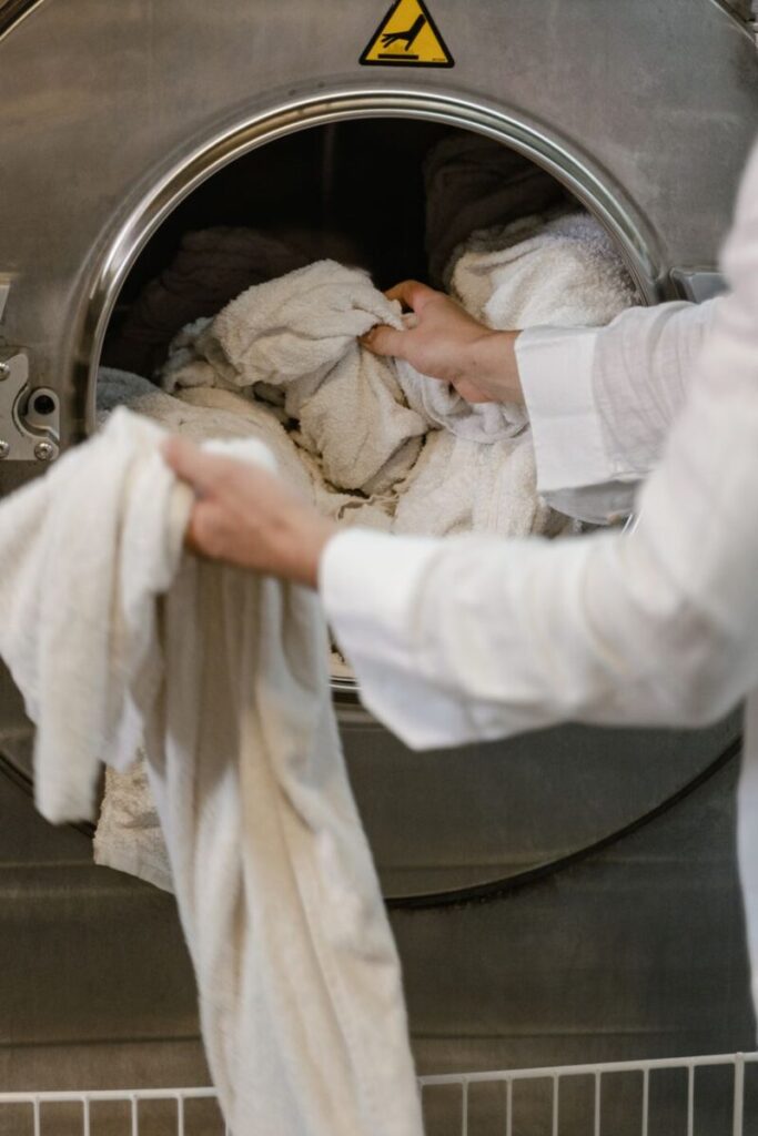 A person loading="lazy" towels into an industrial washing machine in a launderette.