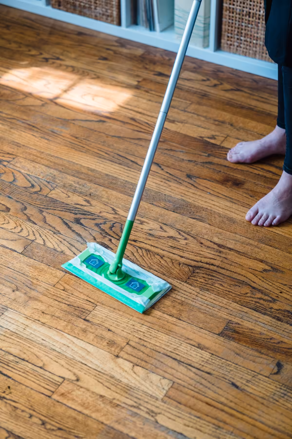 Person sweeping a wooden parquet floor with a green mop, indoors.